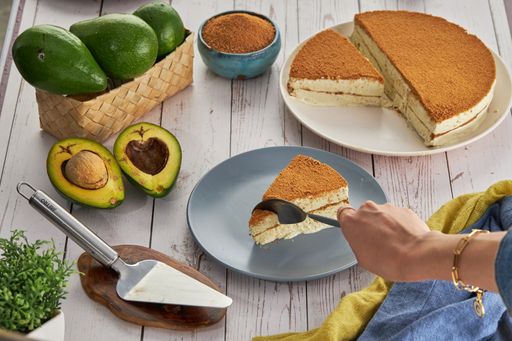 A closeup shot of a hand slicing a piece of cake, avocados, and other ingredients