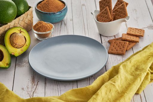 A closeup shot of an empty plate, avocados, cookies, and other ingredients