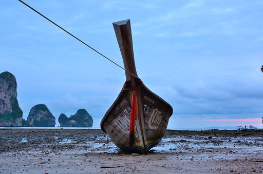 A closeup shot of a boat in low tide ocean with a rock and blue cloudy sky as background