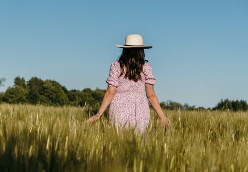 Lifestyle image of beautiful woman with long hair, walking in field and touching wheat or barley ea