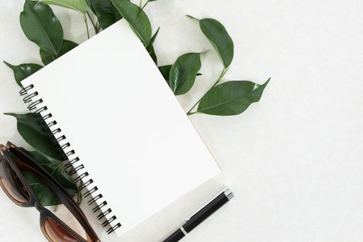 A home office desk table with a houseplant, paper notebook, pen and glasses