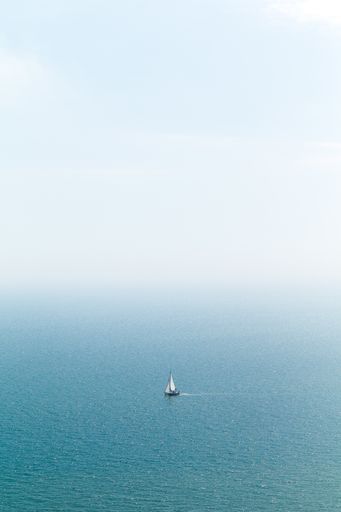 A vertical shot of a sail in the blue sea with a white sky