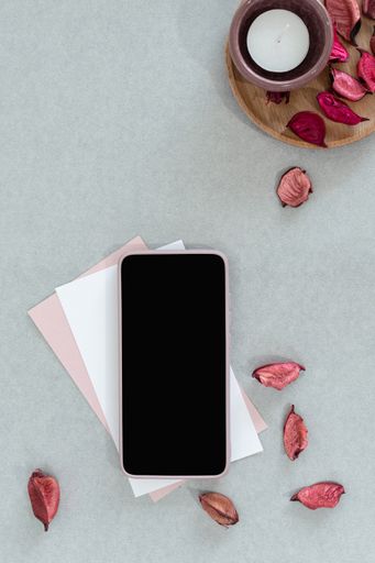 A top view of a phone on envelopes with a candle and autumn leaves on the gray surface