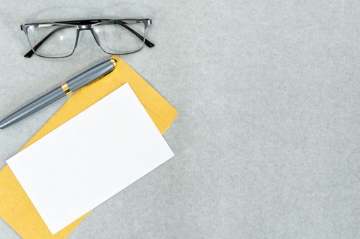 A top view of envelopes with a pen and eyeglasses on a gray surface with space for text