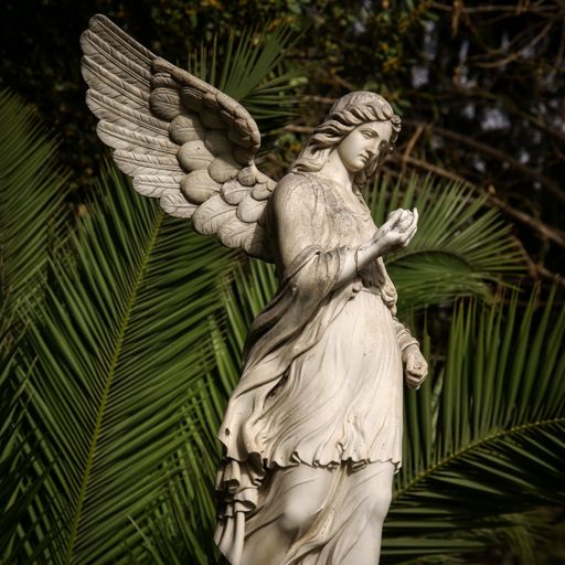 A white angel statue with tropical trees on the background in the park