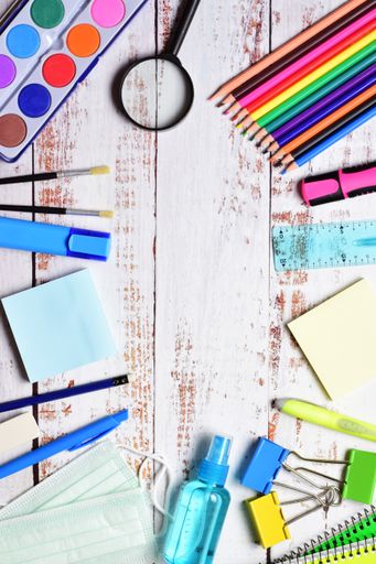 A top view of stationery isolated on a white wooden background. The magnifying glass, watercolor, pencils, brushes, masks, and clips