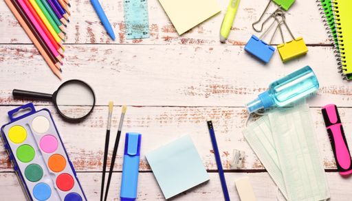 A top view of stationery isolated on a white wooden background. The magnifying glass, watercolor, pencils, brushes, masks, and clips