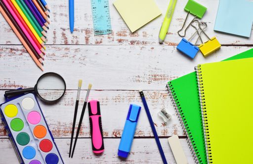 A top view of stationery isolated on a white wooden background. The magnifying glass, watercolor, pencils, brushes, masks, and clips