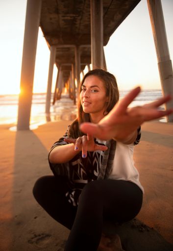 A young beautiful woman from the US reaching for the camera on the sandy beach at golden sunset