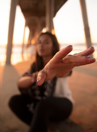 A selective-focus shot of the g=hand of a woman reaching for the camera on a sandy beach at sunset