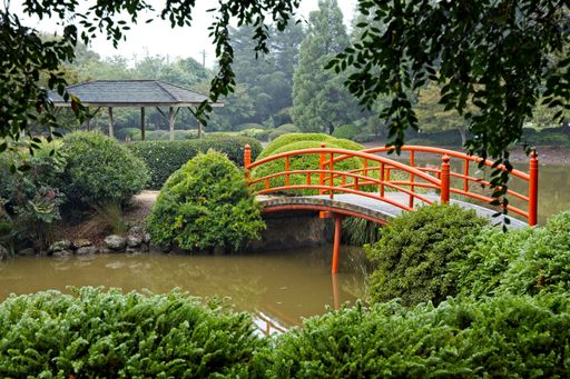 A small red bridge over a pond in a public par