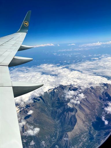A vertical shot of an airplane wing over mountains during its flight to Frankfurt