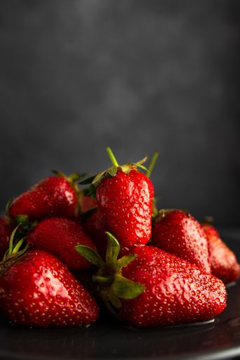 A vertical shot of a pile of fresh strawberries on a black plate