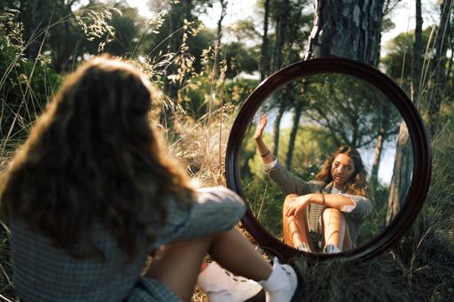 An attractive Caucasian female in a shirt and jeans posing with a mirror on grass