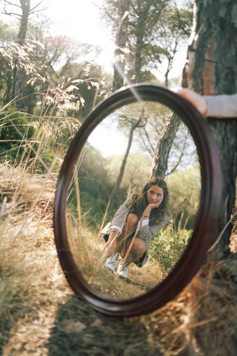 A vertical shot of an attractive Caucasian female in a shirt and jeans posing with a mirror on grass