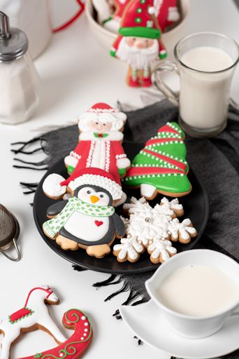 A vertical shot of Christmas sugar cookies on a black plate served with a glass of milk