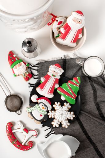 A vertical shot of Christmas sugar cookies on a black plate served with glass of milk