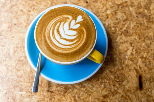 A closeup top view of a cup of cappuccino in a blue plate with a spoon on the table