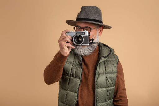 A closeup shot of a bearded man taking a picture with a camera on a brown background