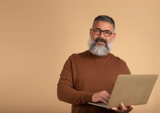 A closeup shot of a bearded man with a laptop on a brown background