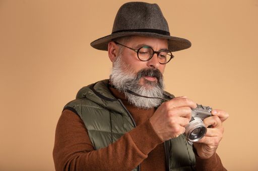 A closeup shot of a bearded man with a camera on a brown background