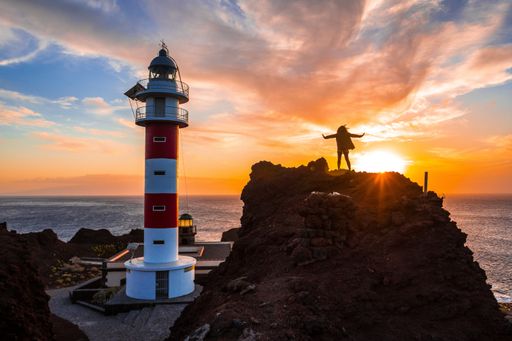 A beautiful view of a person standing on a big rock by the Punta De Teno Lighthouse in Tenerife, Spain