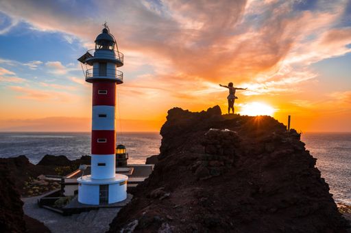 A beautiful view of a person standing on a big rock by the Punta De Teno Lighthouse in Tenerife, Spain