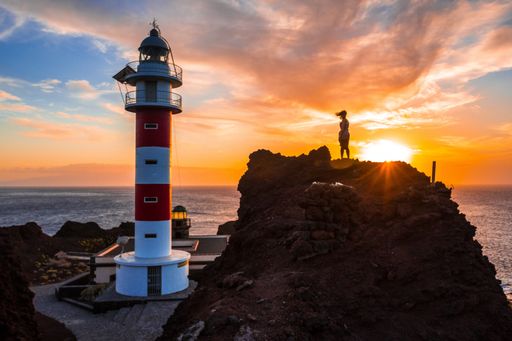 A beautiful view of a person standing on a big rock by the Punta De Teno Lighthouse in Tenerife, Spain