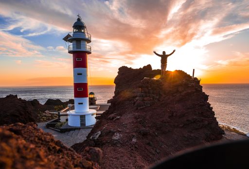 A beautiful view of a person standing on a big rock by the Punta De Teno Lighthouse in Tenerife, Spain