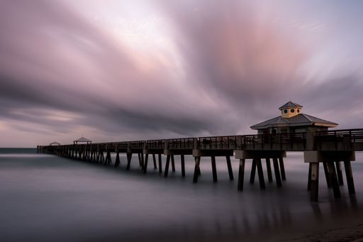 A mesmerizing view of a pier over the sea under a dramatic sunset sky