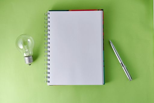 A top view of a light bulb with a notebook and a pen on the green surface