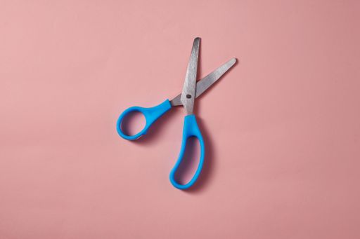A top view of the blue scissors on the pink surface
