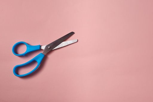 A top view of the blue scissors on the pink surface