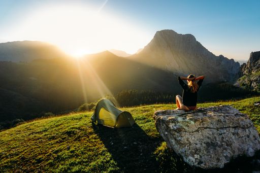 A serene view of a female hiker greeeting the sunrise on top of the mounatins