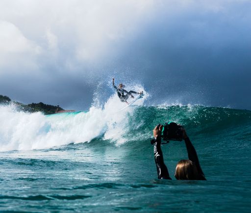 A surfer taking a picutre of his friend surfing the foamy wave of the ocean