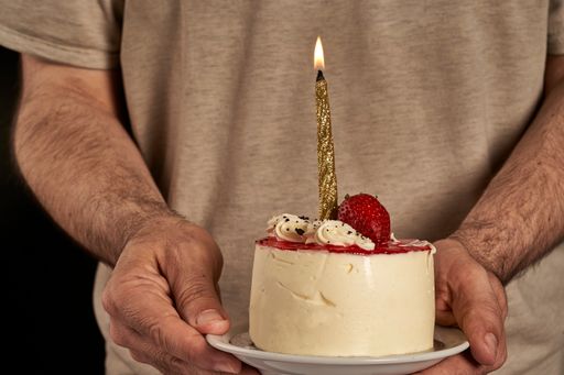 A man's hands bringing a cheesecake with strawberries and a lit candle