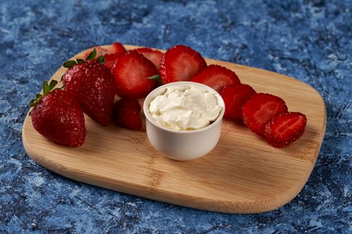 A closeup shot of sliced strawberries and cream cheese on a wooden board