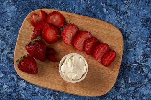 A top view of sliced strawberries and cream cheese on a wooden board
