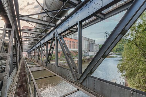 View of an abandoned power plant from a bridge with gas pipes over a river. dramatic sky