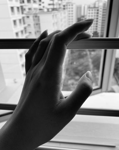 A grayscale shot of a delicate hand of a woman resting on a window in the daylight
