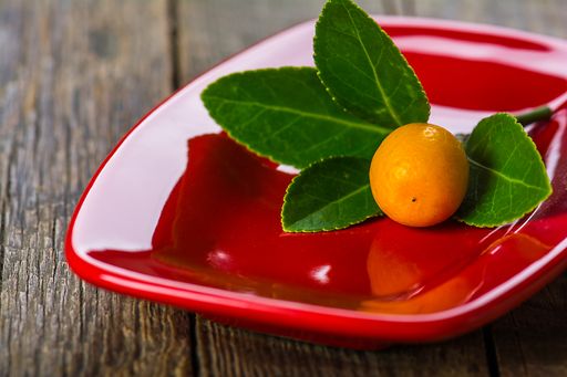 Ripe kumquat fruit on a red plate on a wooden table