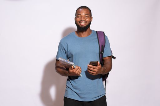 A smiling African male student standing against a white wall