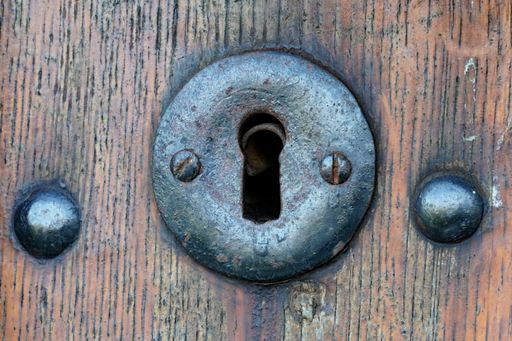 A close up of an old forged metal keyhole on an old wooden door