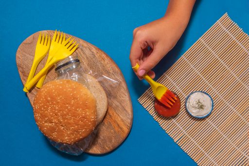 A top view of a burger with plastic in it and a hand next to it - pollution concept