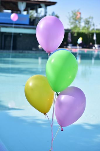 A close up pf a cluster of colorful balloons with a pool in the background on a sunny day