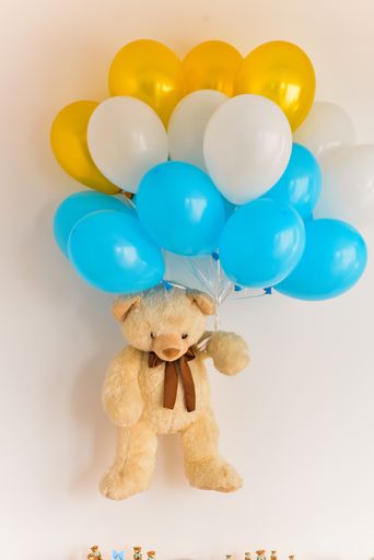 A close up shot of a bear toy holding colorful balloons and held on the wall