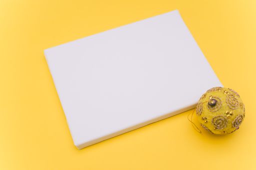 Elegant yellow silver Christmas decorations and painting canvas with sapce for text on a yellow tabletop surface