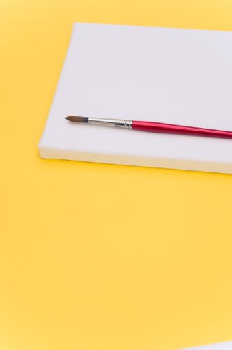 top view shot of blank white paint canvas and tools on a yellow paper surface with copy space