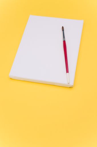 top view shot of blank white paint canvas and tools on a yellow paper surface with copy space