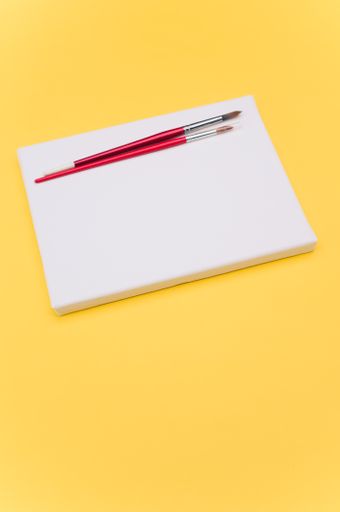 top view shot of blank white paint canvas and tools on a yellow paper surface with copy space